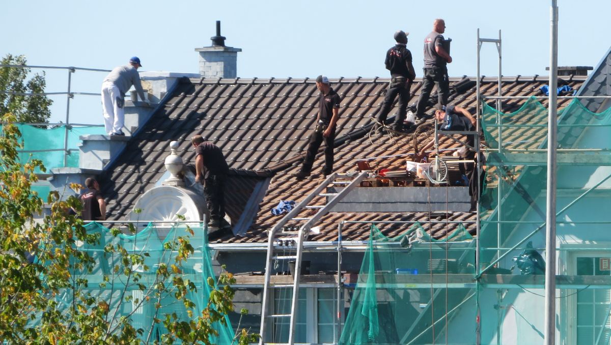 Dakdekkers vervangen pannen op een woning, met een stelling langs de gevel